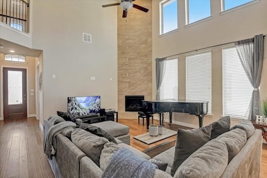 Living room featuring light wood-style flooring, a high ceiling, a high end fireplace, and a ceiling fan
