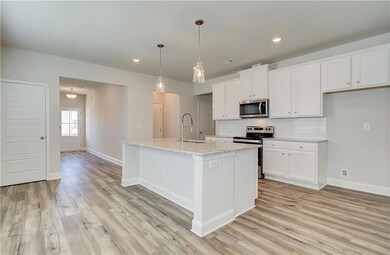 Kitchen featuring appliances with stainless steel finishes, backsplash, white cabinetry, hanging light fixtures, and a kitchen island with sink