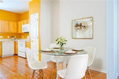 Kitchen with light brown cabinets, light wood-style flooring, white appliances, light countertops, and baseboards