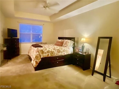 Bedroom featuring a tray ceiling, light carpet, and ceiling fan