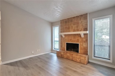 Unfurnished living room with wood finished floors, plenty of natural light, a fireplace, and a textured ceiling