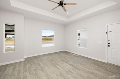 Spare room with a tray ceiling, wood tiled floors, healthy amount of natural light, ceiling fan, and recessed lighting