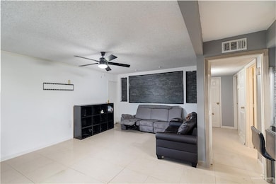 Living area with ceiling fan, a textured ceiling, and light tile patterned floors