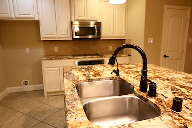Kitchen featuring light stone countertops, stainless steel microwave, light tile patterned floors, and decorative backsplash