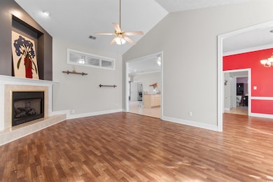 Unfurnished living room featuring light wood-type flooring, ceiling fan, a tiled fireplace, vaulted ceiling, and ornamental molding
