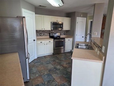 Kitchen with backsplash, stainless steel appliances, light countertops, white cabinets, and stone finish floors