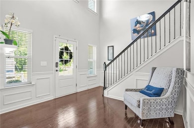 Foyer entrance featuring a decorative wall, stairs, a wainscoted wall, dark wood-type flooring, and a high ceiling