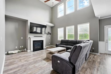 Living area featuring ceiling fan, wood finished floors, high vaulted ceiling, and a glass covered fireplace