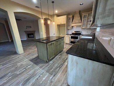 Kitchen featuring green cabinets, custom exhaust hood, stainless steel range with electric stovetop, glass insert cabinets, and arched walkways