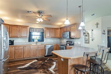 Kitchen featuring appliances with stainless steel finishes, a peninsula, a breakfast bar area, a ceiling fan, and dark wood-style floors