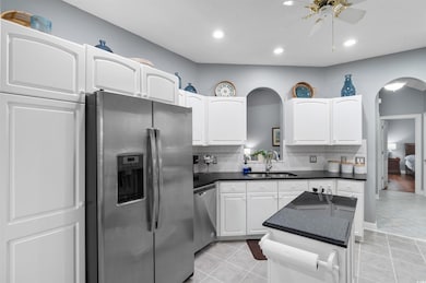 Kitchen featuring stainless steel appliances, arched walkways, dark countertops, a center island, and a ceiling fan