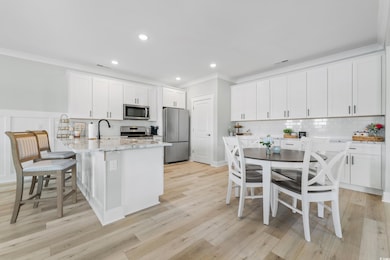 Kitchen with white cabinetry, ornamental molding, a peninsula, light stone countertops, and appliances with stainless steel finishes