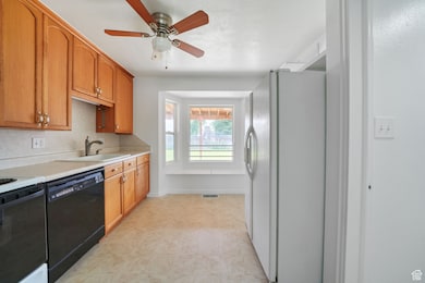 Kitchen featuring freestanding refrigerator, dishwasher, light countertops, ceiling fan, and brown cabinets