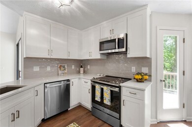 Kitchen with stainless steel appliances, white cabinets, light countertops, dark wood finished floors, and tasteful backsplash