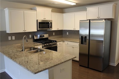 Kitchen with stainless steel appliances, white cabinetry, light stone counters, a peninsula, and dark wood finished floors