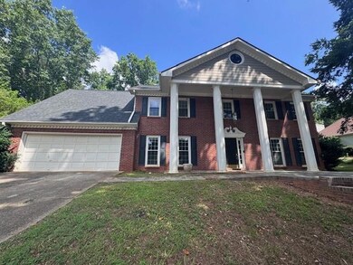 Neoclassical / greek revival house with concrete driveway, an attached garage, brick siding, and a front yard