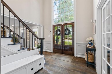 Entrance foyer with french doors, dark wood finished floors, stairway, a decorative wall, and wainscoting