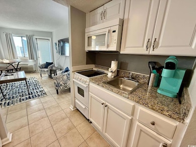 Kitchen with white cabinets, light tile patterned flooring, white appliances, a textured ceiling, and light stone counters