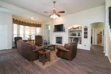 Graceful arches repeat above the hallway entry and the built-in shelving to the right of the gas log fireplace with a tile surround and custom milled mantle.  An expansive bay window with 2 inch blinds and designer valences covers the back wall.