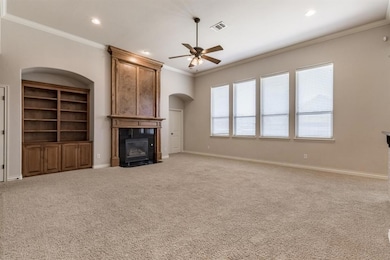 Unfurnished living room featuring a ceiling fan, a tiled fireplace, arched walkways, ornamental molding, and baseboards