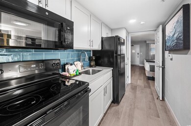 Kitchen with black appliances, white cabinets, backsplash, and light hardwood / wood-style flooring