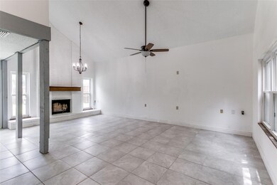 Living room featuring brick wall, light tile flooring, a fireplace, ceiling fan with notable chandelier, and high vaulted ceiling