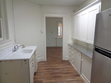 Kitchen with freestanding refrigerator, dark wood-style floors, light countertops, and white cabinetry