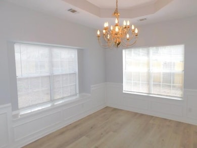 Empty room with a chandelier, a decorative wall, light wood-style floors, and wainscoting
