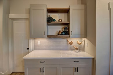 Kitchen featuring open shelves, backsplash, light stone countertops, and cabinetry.Tour and photos are a depiction of the Primrose plan