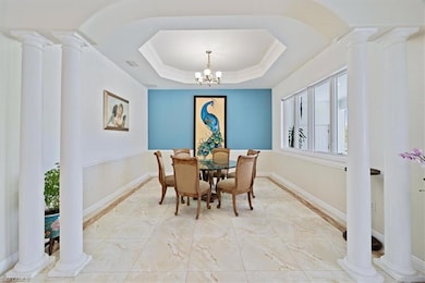 Dining area with light tile flooring, decorative columns, ornamental molding, baseboards, and a raised ceiling