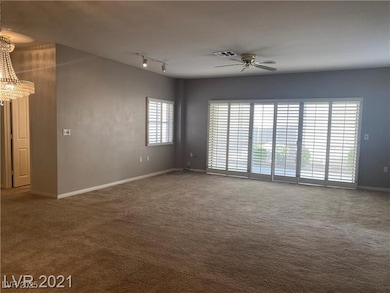 Carpeted empty room with baseboards, track lighting, and ceiling fan with notable chandelier