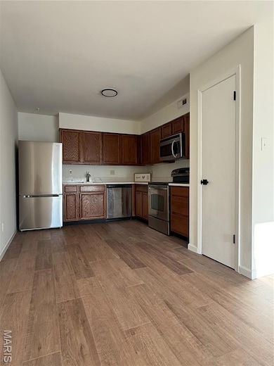Kitchen featuring quartz countertops, appliances with stainless steel finishes, light wood-style flooring, and dark brown cabinetry