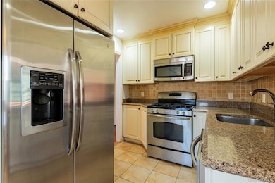 Kitchen featuring appliances with stainless steel finishes, light tile patterned floors, dark stone counters, decorative backsplash, and recessed lighting