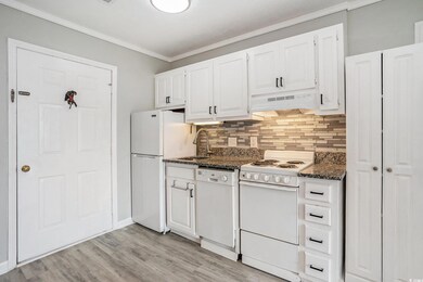Kitchen featuring white appliances, white cabinetry, crown molding, under cabinet range hood, and backsplash