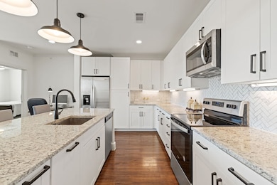 Kitchen with stainless steel appliances, dark wood finished floors, decorative backsplash, light stone counters, and hanging light fixtures