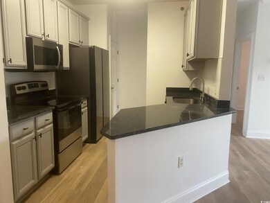 Kitchen featuring appliances with stainless steel finishes, light wood-style flooring, dark stone counters, and a peninsula