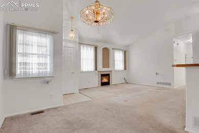 Unfurnished living room featuring carpet flooring, lofted ceiling, a fireplace, a chandelier