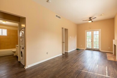 Unfurnished living room with stacked washing machine and dryer, dark wood-style flooring, ceiling fan, and french doors
