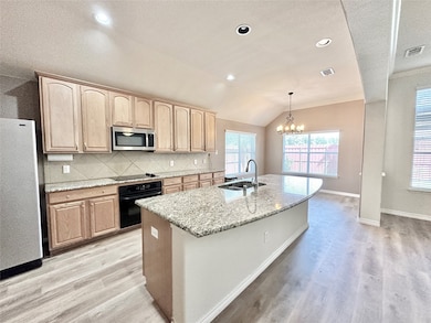 Kitchen with tasteful backsplash, black appliances, an island with sink, lofted ceiling, and decorative light fixtures