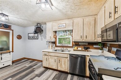 Kitchen with black stainless steel appliances, glazed cabinets, countertops, wood finished floors, and a textured ceiling