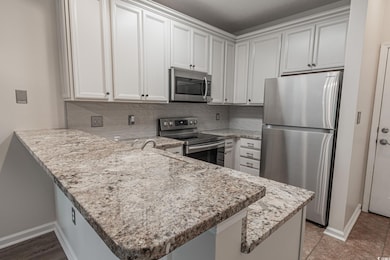 Kitchen featuring stainless steel appliances, a peninsula, tasteful backsplash, white cabinetry, and light stone counters