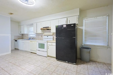 Kitchen featuring white appliances, light countertops, white cabinets, tasteful backsplash, and a textured ceiling