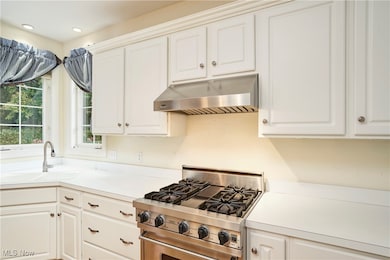 Kitchen with designer stove, under cabinet range hood, white cabinets, and light countertops
