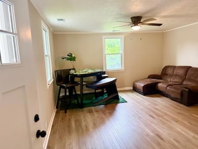 Living area with wood finished floors, a ceiling fan, baseboards, a textured ceiling, and crown molding