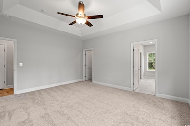 Unfurnished bedroom with a tray ceiling, light carpet, ceiling fan, and connected bathroom
