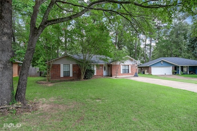 Ranch-style house featuring concrete driveway, brick siding, and view of wooded area