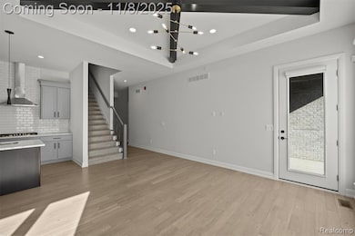 Unfurnished living room with light wood-type flooring, a chandelier, a raised ceiling, stairway, and recessed lighting