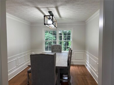 Dining room featuring dark wood-style floors, a decorative wall, a wainscoted wall, ornamental molding, and a textured ceiling
