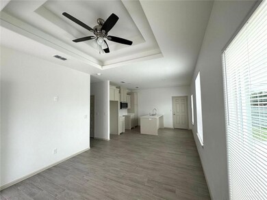 Unfurnished living room featuring visible vents, ceiling fan, baseboards, light wood-type flooring, and a tray ceiling