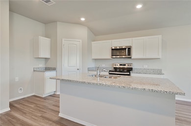 Kitchen featuring white cabinetry, light stone counters, stainless steel appliances, light wood-style floors, and lofted ceiling